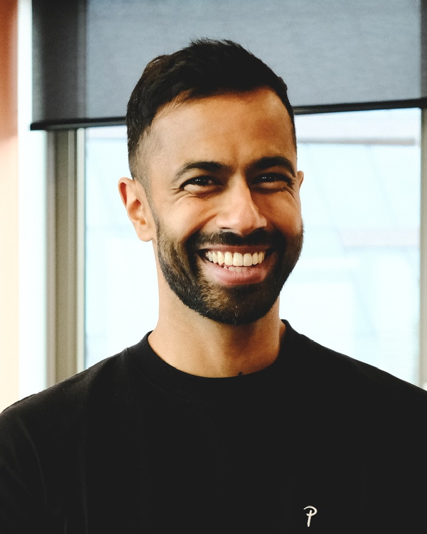 Prem Mistry, smiling, in a black T-shirt in a studio with a warm peach wall